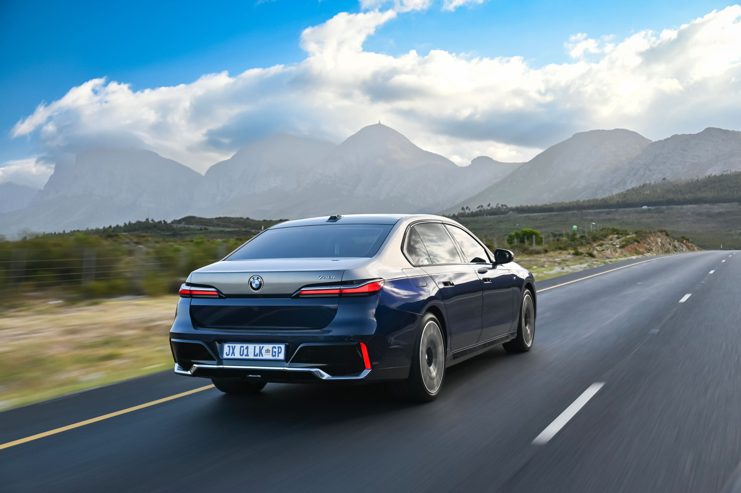 BMW 7 Series (G70) 740i driving on a country road. Rear three-quarter view.