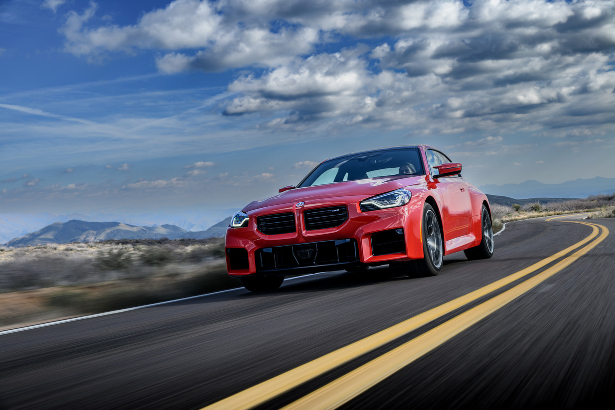 2023 BMW M2 coupe driving on a country road, front three-quarter view.